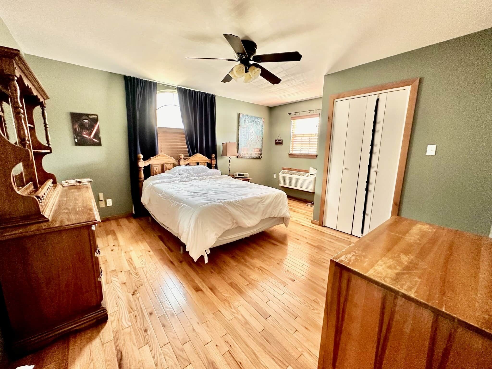 Un dormitorio con cama, cómoda de madera, ventilador de techo y ventana con cortinas.