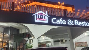 Café y restaurante con letrero de Casa de Huéspedes, con un diseño arquitectónico moderno, ventanas de vidrio y un balcón decorado con luces colgantes.