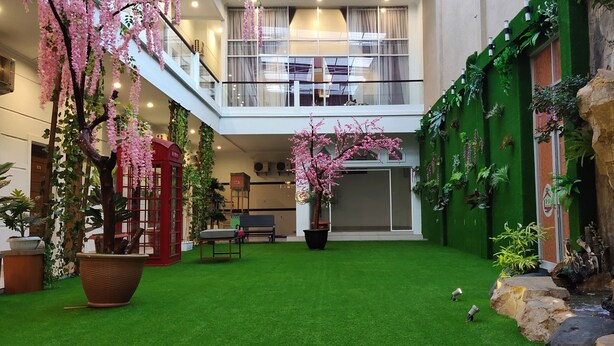 Un jardín interior amplio con césped artificial, plantas en macetas, un teléfono rojo y una cascada.