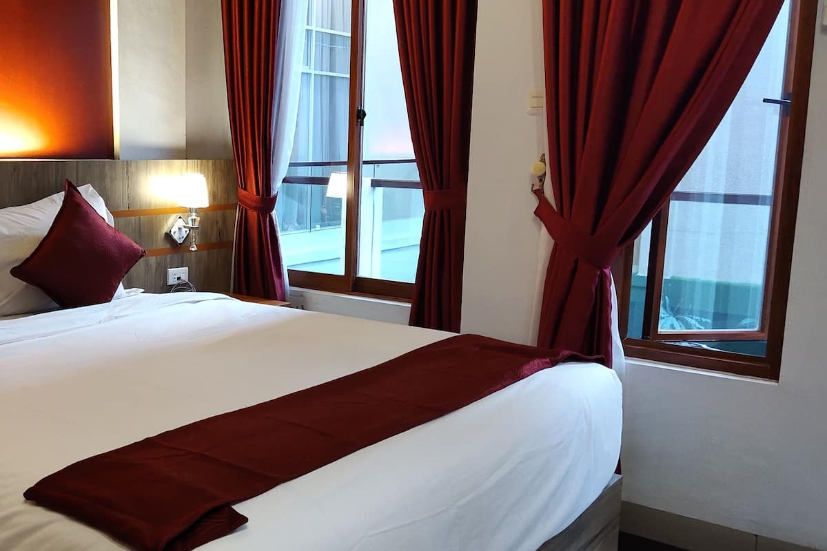 Une chambre d’hôtel avec un grand lit, des rideaux rouges, une lampe de chevet et une vue sur l’extérieur.