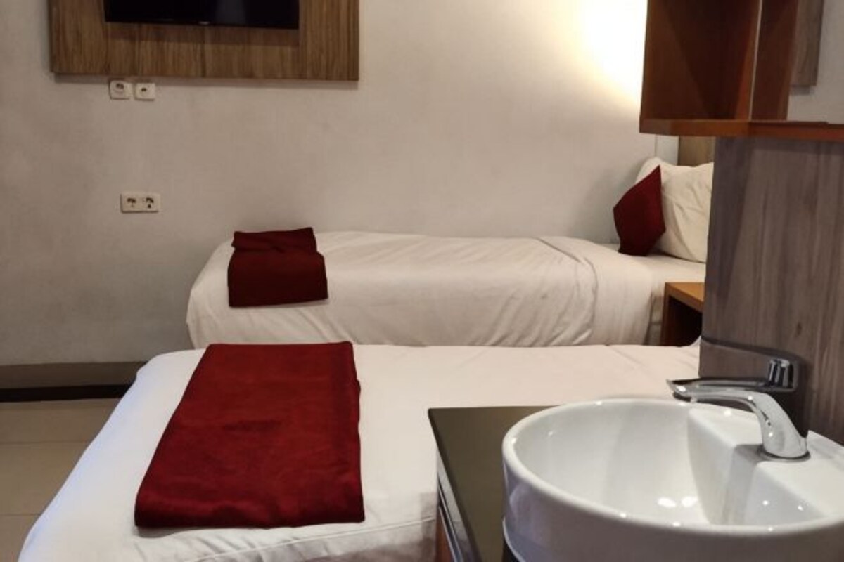 A hotel room with two beds, a white sink, and a mirror above it.