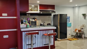 Cocina compacta con una pared de acento roja, un refrigerador negro, una estufa a gas y una pequeña barra con taburetes.
