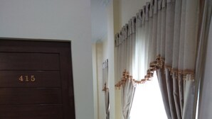 Un pasillo con una puerta marcada '415', que conduce a una habitación con cortinas y un ventanal.