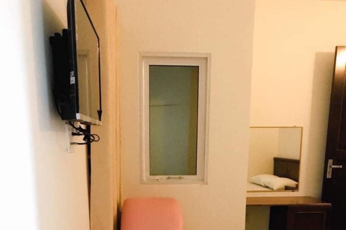A small room with a bed, a chair, a desk, a mirror, and a television.