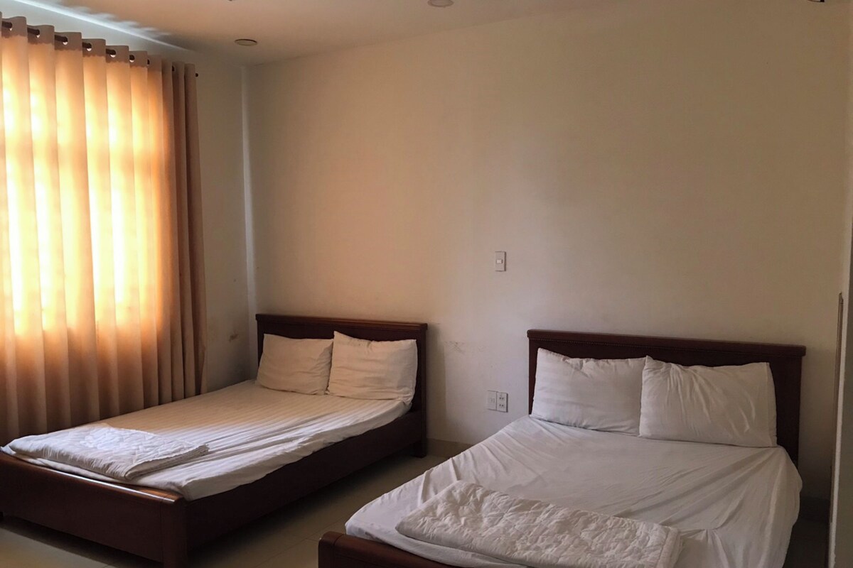 Two single beds with wooden frames and white bedding in a room with a plain wall and a window with curtains.