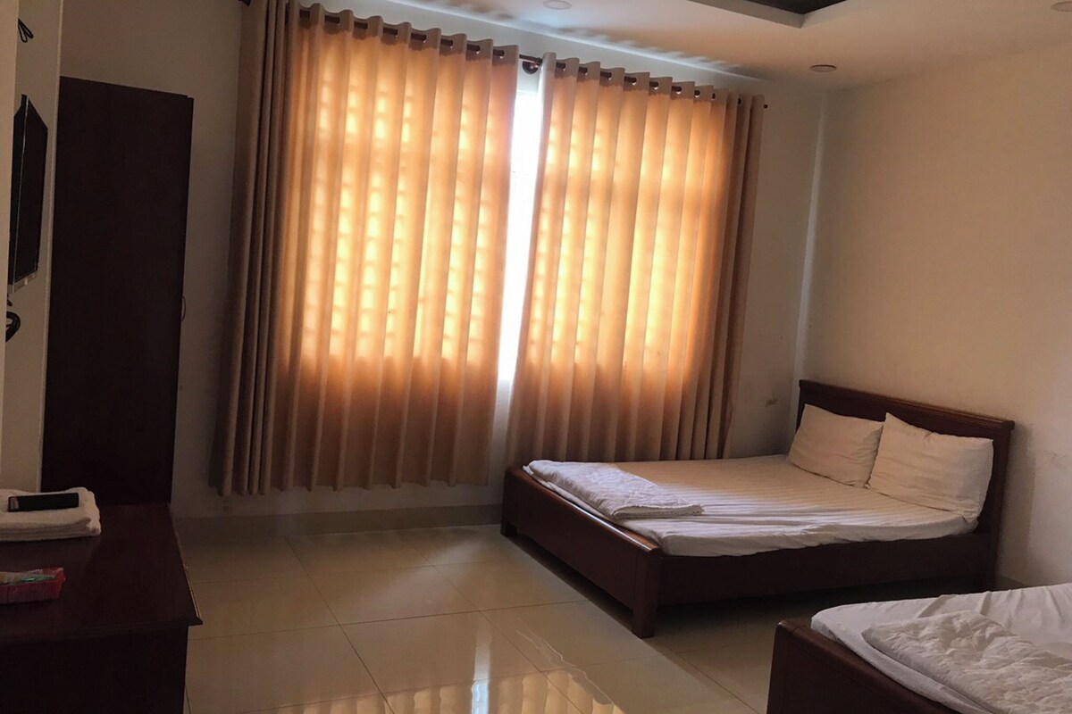 Une chambre d’hôtel avec un lit, une table de chevet, une armoire et une fenêtre avec des rideaux.