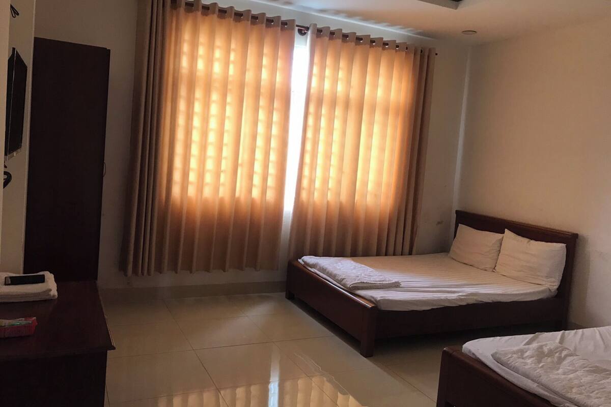 Ein Hotelzimmer mit Bett, Nachttisch, Schrank und einem Fenster mit Vorhängen.