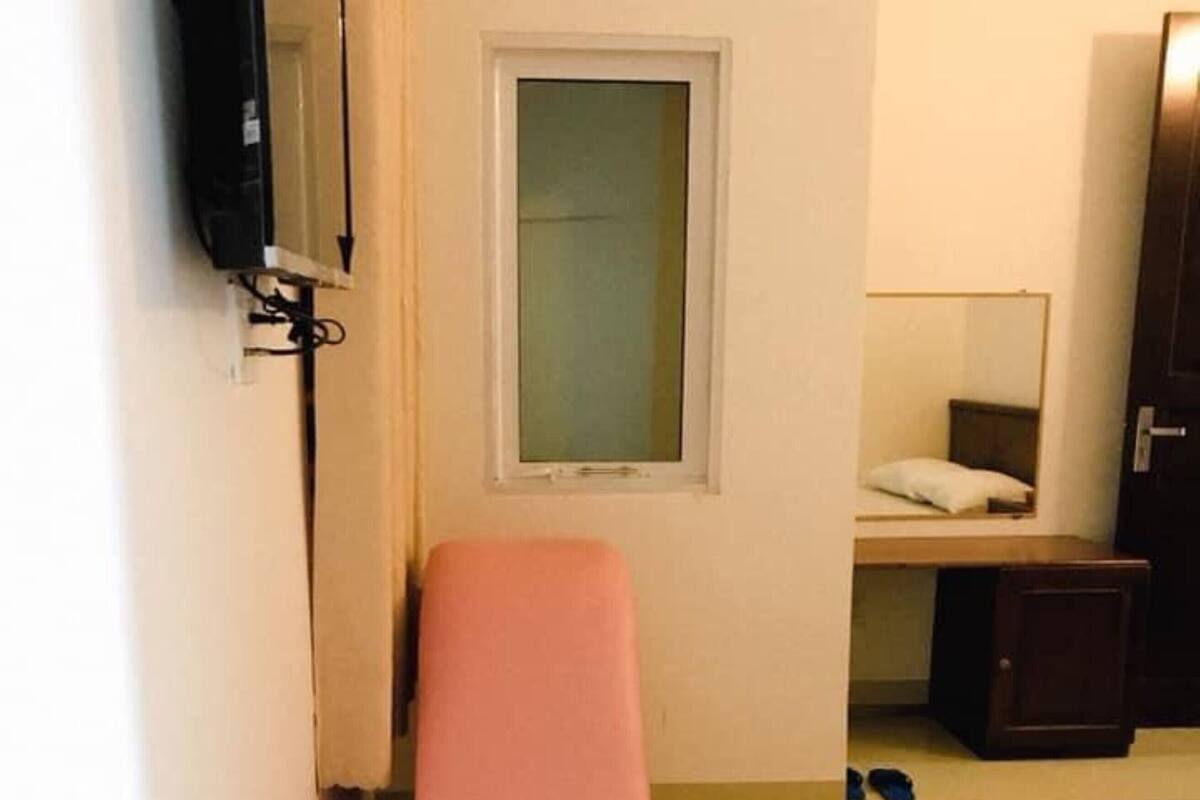 Ein kleines Zimmer mit einem Bett, einem Sessel, einem Schreibtisch, einem Spiegel und einem Fernseher.