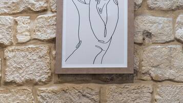 Une illustration linéaire encadrée sur un mur de pierre, un canapé noir avec un coussin turquoise et une table d’appoint noire.