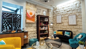 Un salon chaleureux avec un fauteuil jaune, un canapé turquoise, une table basse ronde et une bibliothèque.