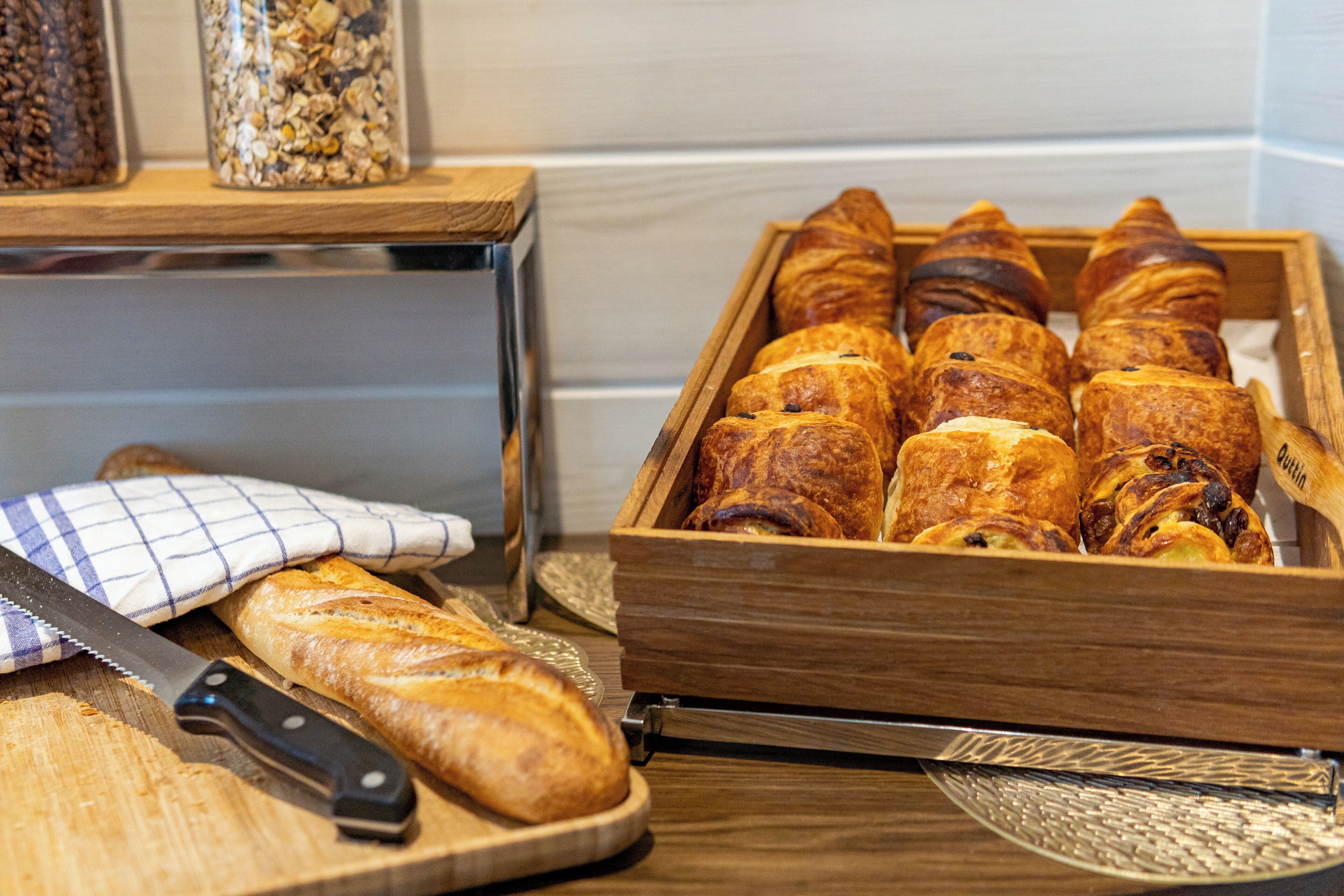 Un plateau de service en bois, sur lequel sont disposés divers pâtisseries, un couteau et une nappe à carreaux, le tout posé sur une table en bois.