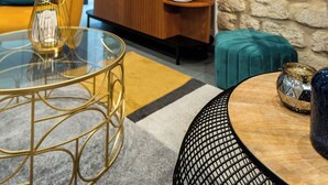 Un salon moderne avec un canapé jaune, une table basse en verre et un mur en pierre orné d’un tableau.