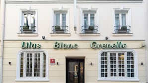 Une façade d’immeuble avec trois fenêtres et l’inscription « Lilas Blanc Grenelle » au-dessus.