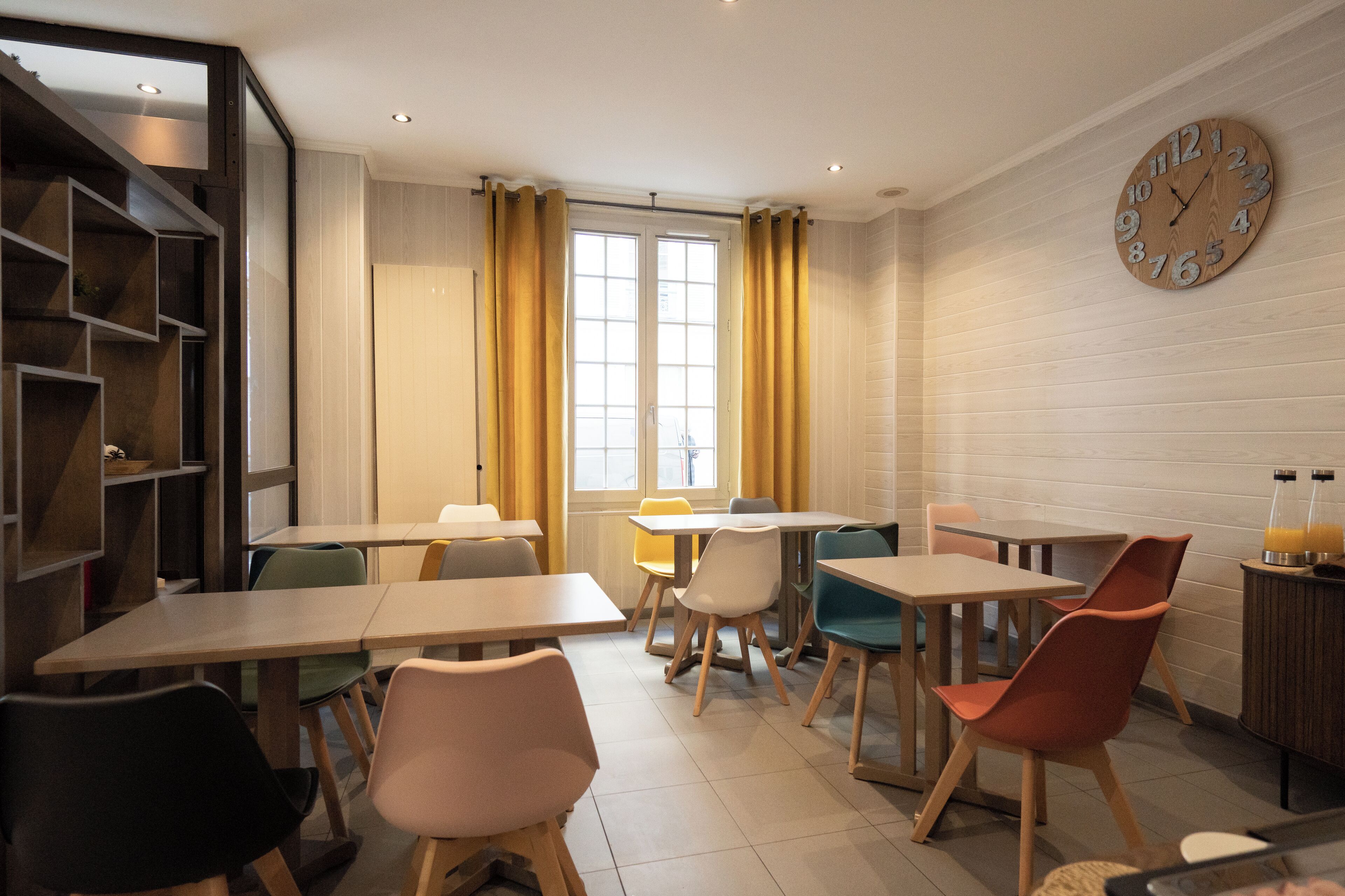 A dining area with tables and chairs, a clock on the wall, and a window with curtains.