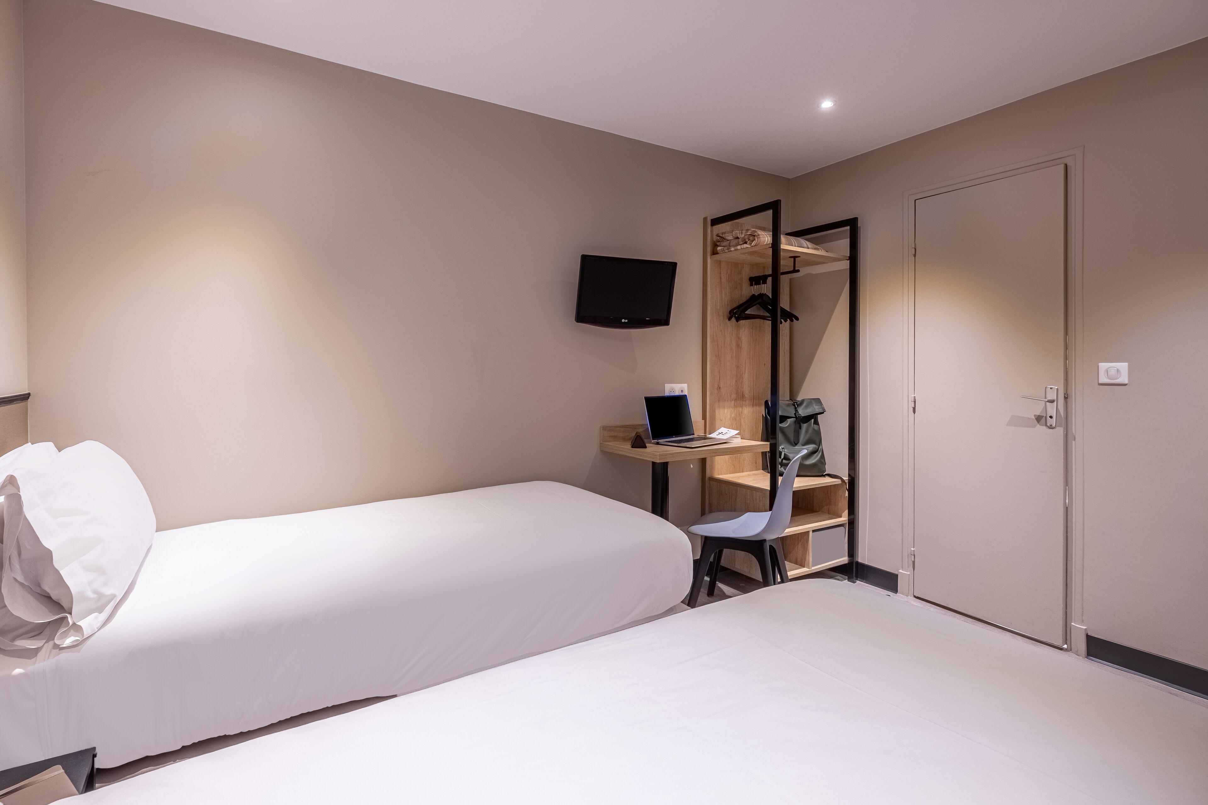 A hotel room with two beds, a desk with a laptop, a chair, a TV mounted on the wall, and a wardrobe.