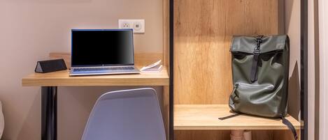 A compact room with a wooden desk, a laptop, a TV, a chair, and a wardrobe with shelves.
