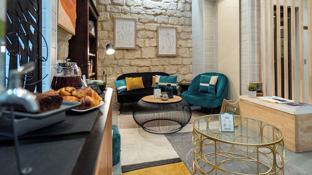 Un coin salon accueillant avec un mur en pierre, un canapé noir agrémenté de coussins turquoise, une table basse ronde et une table en verre avec un cadre doré.