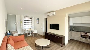A modern living room with a sofa, a round coffee table, a TV, and a kitchen area with a stove and sink. - Renovated Bastide, Capelan peninsula, quiet (Bandol)