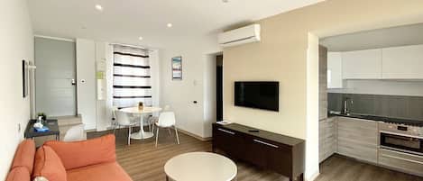 Un soggiorno moderno con un divano, un tavolino rotondo, una TV e un angolo cottura con fornello e lavello.
