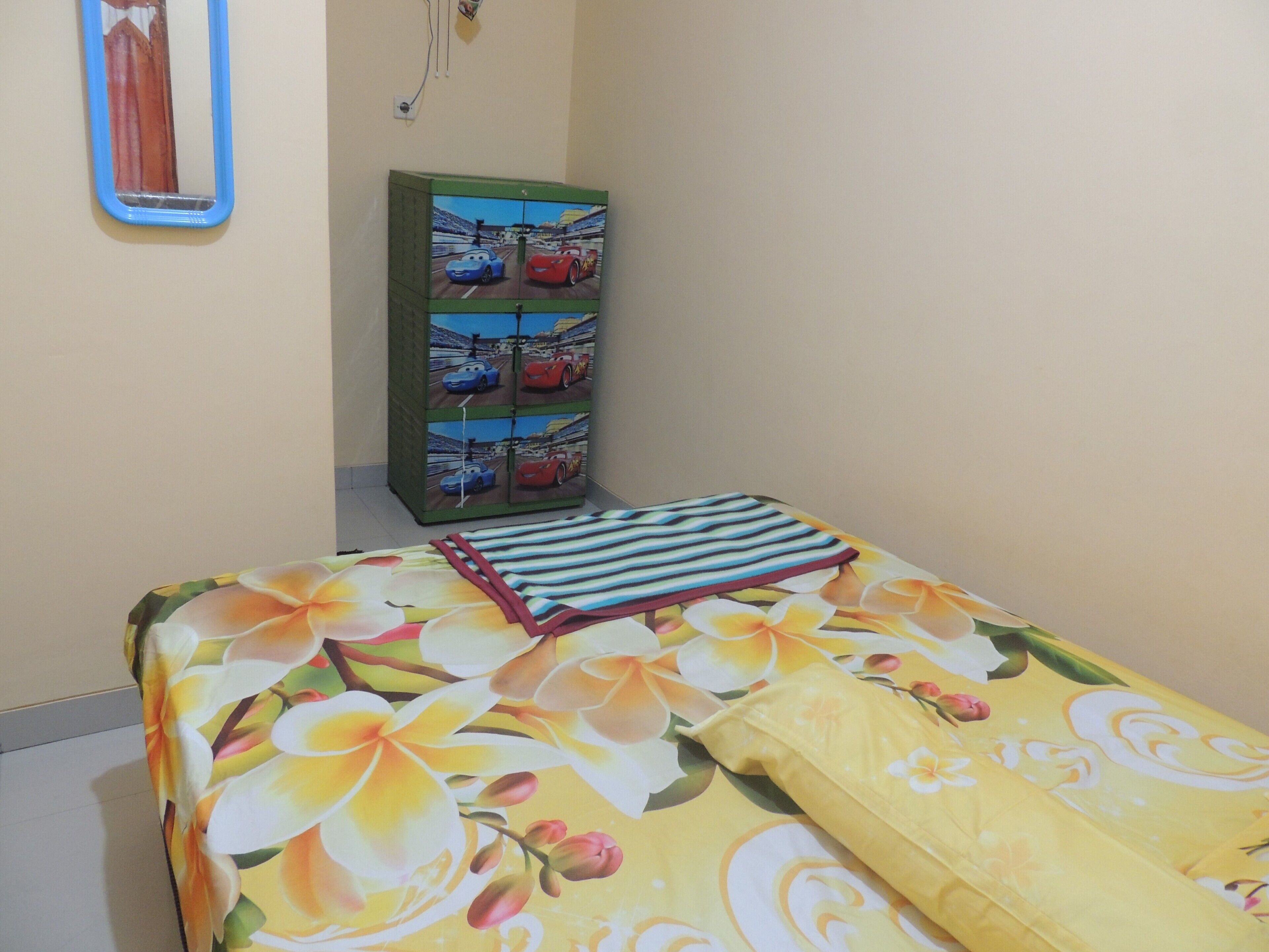 A bedroom with a bed, a green wardrobe with car-themed artwork, and a mirror on the wall.