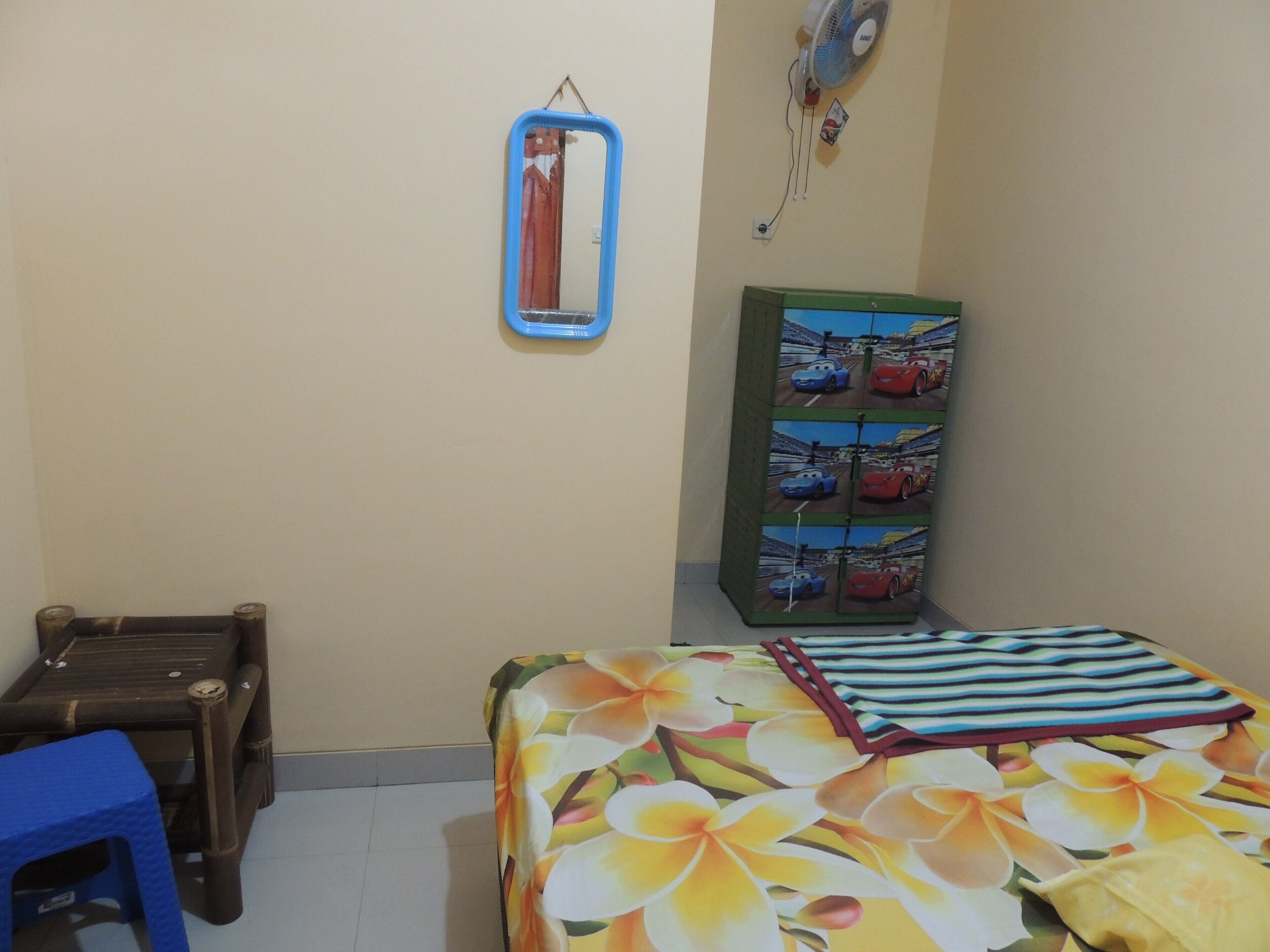 Una habitación con una cama, una silla azul, un armario decorado con calcomanías de autos y un espejo instalado en la pared.