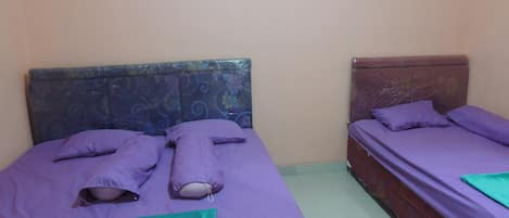 Two single beds with headboards, purple bedding, and a green blanket on the floor.