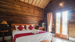 A wooden-paneled bedroom with a bed, a nightstand, a lamp, and a sliding glass door to the outside. - Penida Lapaya Garden (Penida Island)