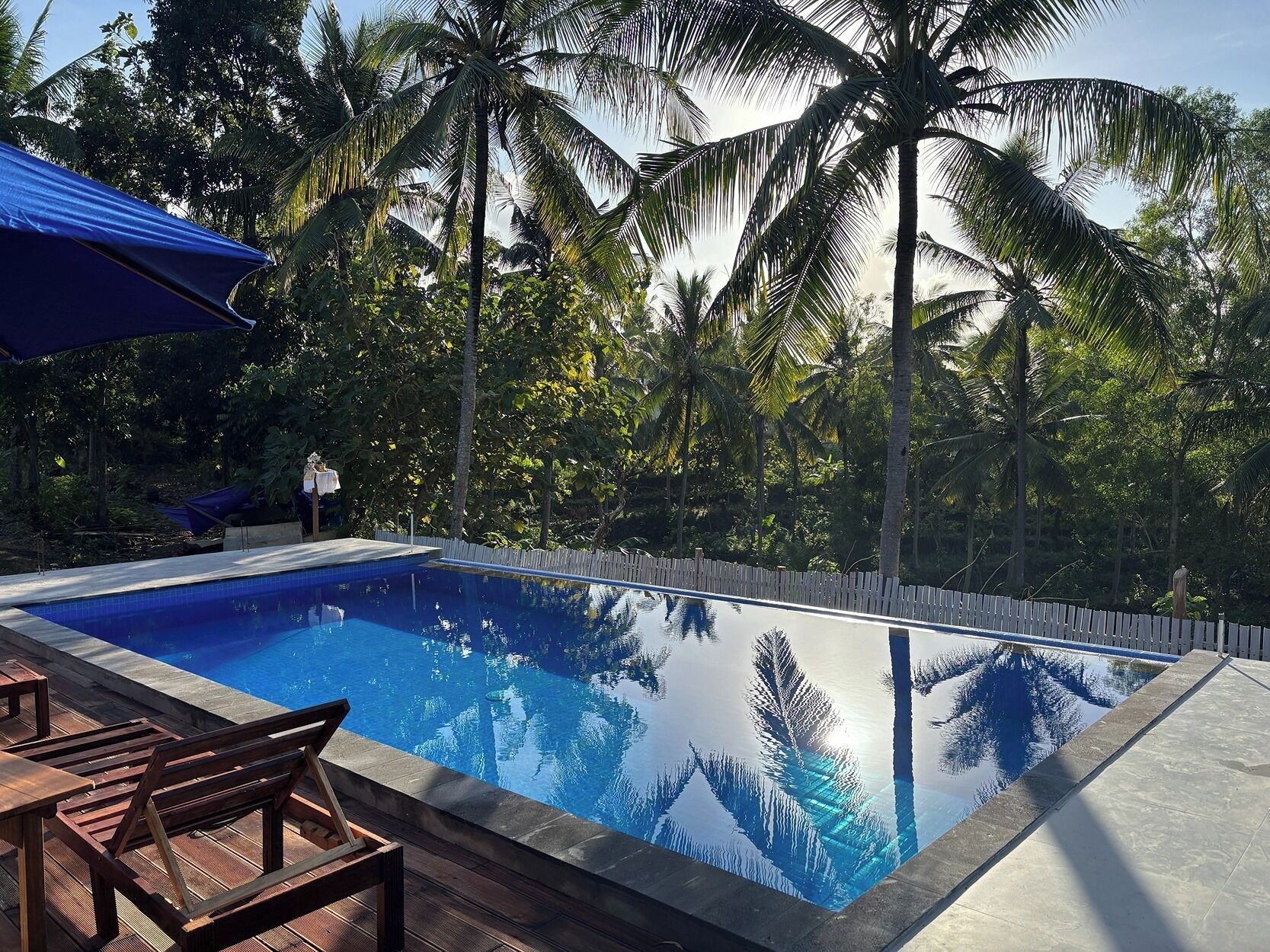 A rectangular swimming pool with clear blue water, surrounded by a wooden deck and a white fence.