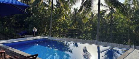 A rectangular swimming pool with clear blue water, surrounded by a wooden deck and a white fence.