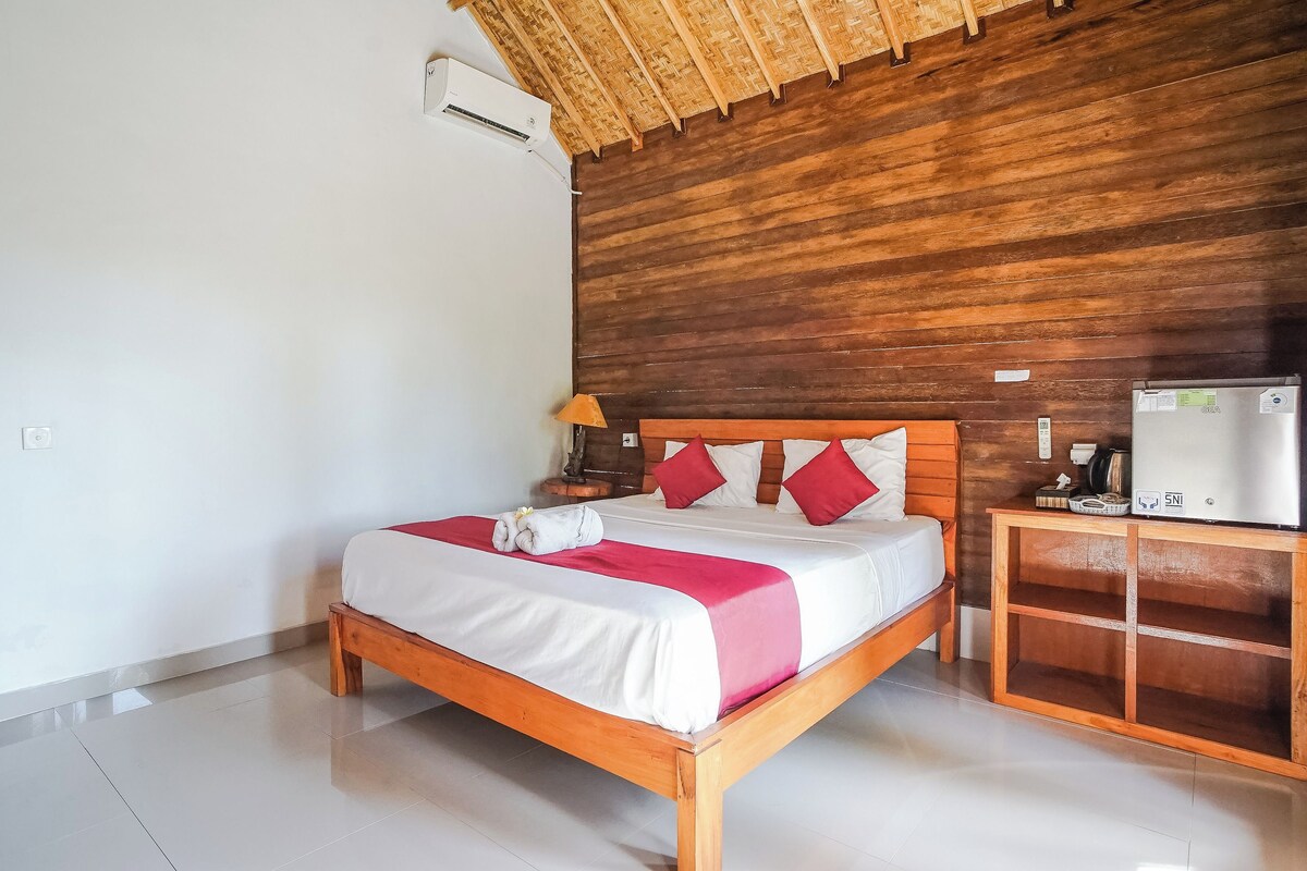 A neatly made bed with a wooden headboard, a bedside table with a lamp, and a minibar.