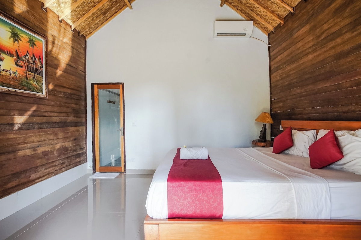 A hotel room with a wooden ceiling, a bed with white and red bedding, and a painting on the wall.
