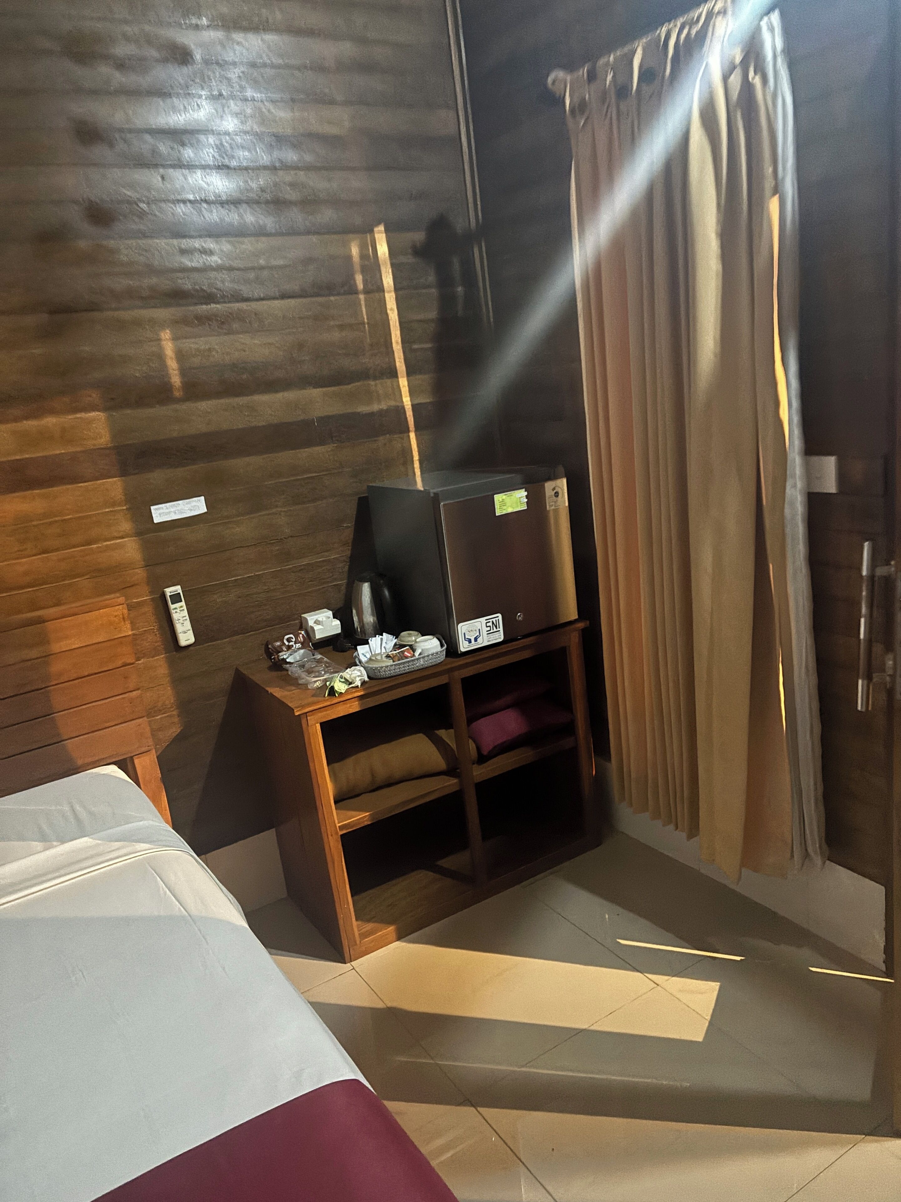 Een hotelkamer met een houten wand, een bed met wit en rode beddengoed, een klein houten tafeltje met een televisie, en een gordijn.