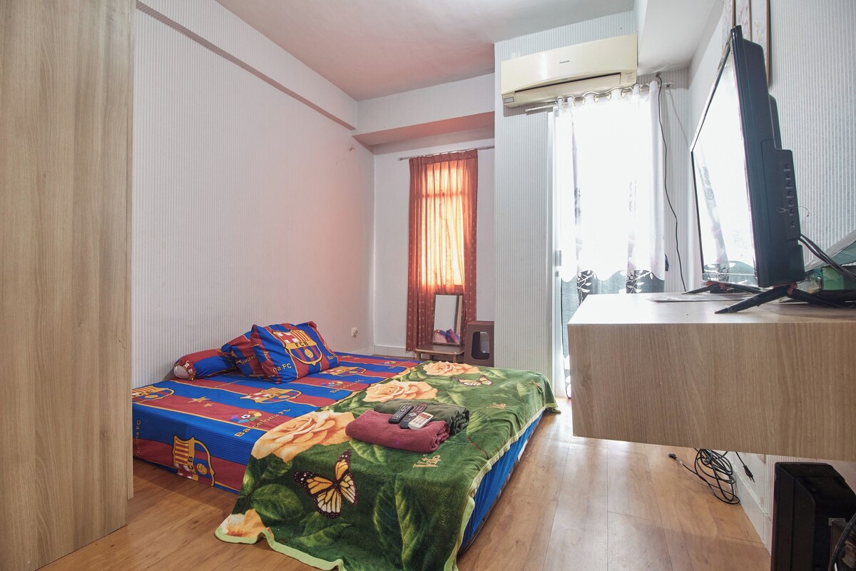 Un dormitorio con cama, escritorio, aire acondicionado, ventana con cortinas y espejo.