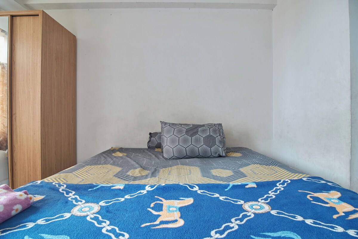 Un dormitorio con una cama, dos almohadas, una manta azul y un armario de madera.