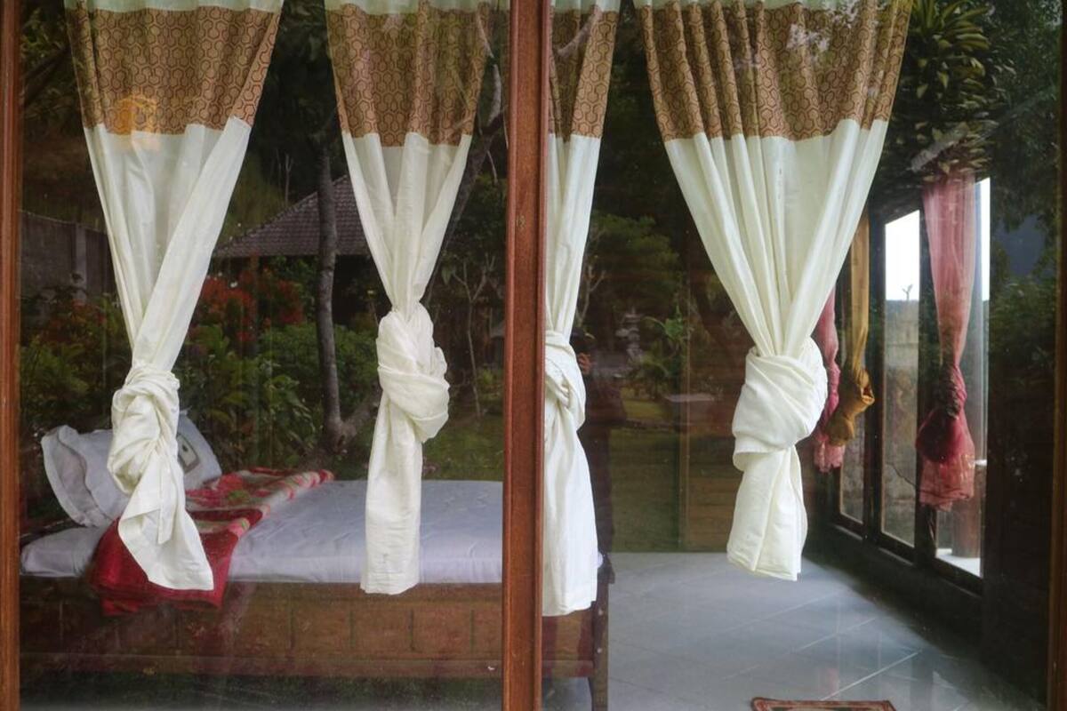 Una habitación con cama, cortinas atadas y vistas a zonas verdes.