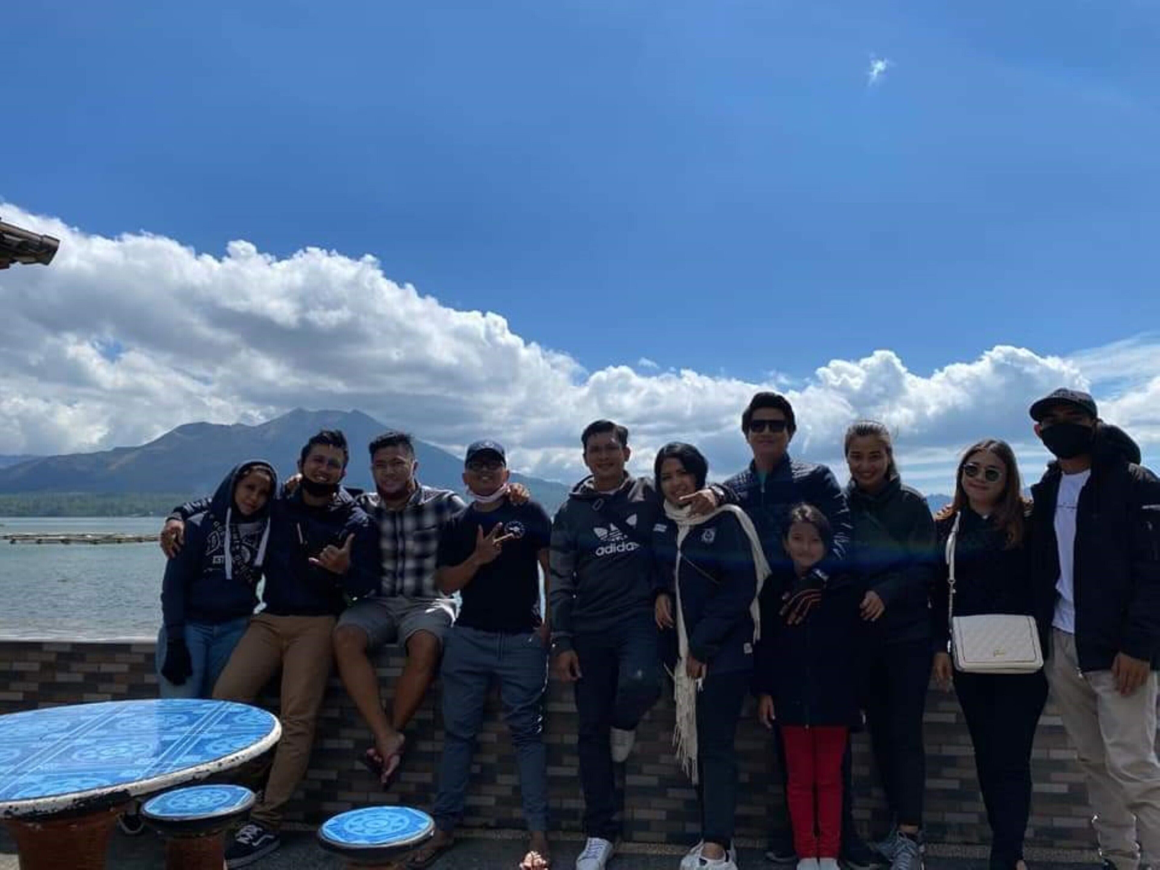 A group of people posing by a body of water with mountains in the background.