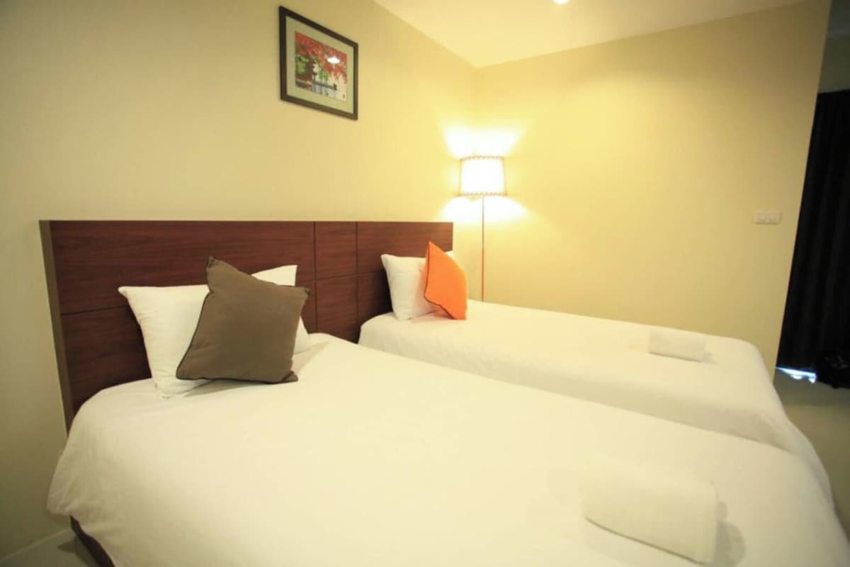 Habitación de hotel con dos camas, cada una con sábanas y almohadas blancas, cabeceros de madera y una lámpara fijada a la pared.