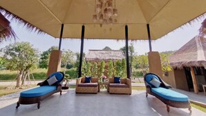Un espacio de estar al aire libre cubierto con sillones de mimbre y un edificio de techo de paja al fondo.