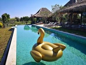 Relax by the serene pool surrounded by lush greenery and a thatched-roof structure.