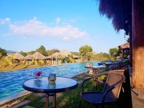 Guests can enjoy a serene poolside setting surrounded by lush greenery and thatched-roof accommodations.