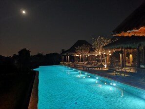 A nighttime swimming pool area with lounge chairs and umbrellas, surrounded by trees and a mountain in the background. - Hideaway (Hang Dong)