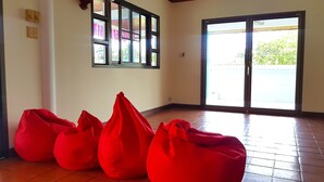 Una habitación con suelo de baldosas, un ventanal con cortinas y varios sillones de felpa rojos.