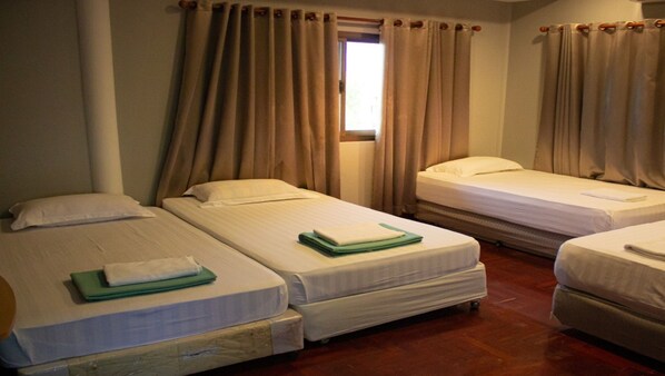 A hotel room with three single beds, a window with curtains, and a wooden floor.