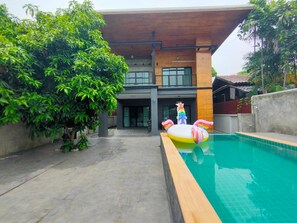 A modern house with a swimming pool, surrounded by lush greenery.