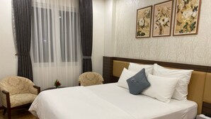 A hotel room with a large bed, two armchairs, a small table with a vase, and three framed floral pictures on the wall.