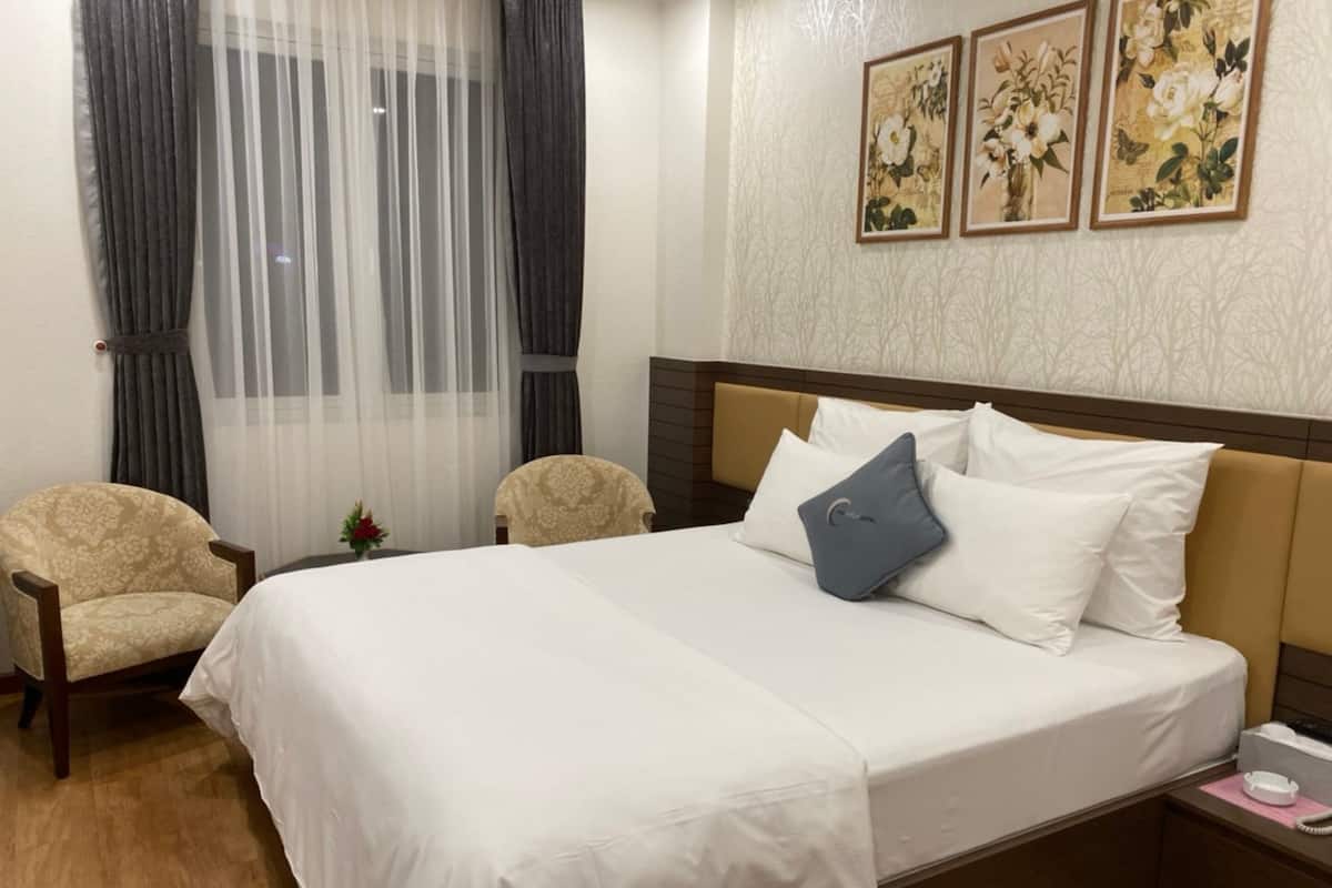 Ein Hotelzimmer mit einem großen Bett, zwei Sesseln, einem kleinen Tisch mit einer Vase und drei gerahmten Blumenbildern an der Wand.