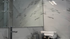 A modern bathroom with a round white sink, a glass shower enclosure, and a marble backsplash.