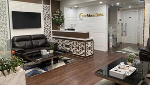 A hotel reception area with a modern design, featuring a reception desk, a black leather sofa, and a coffee table with amenities.