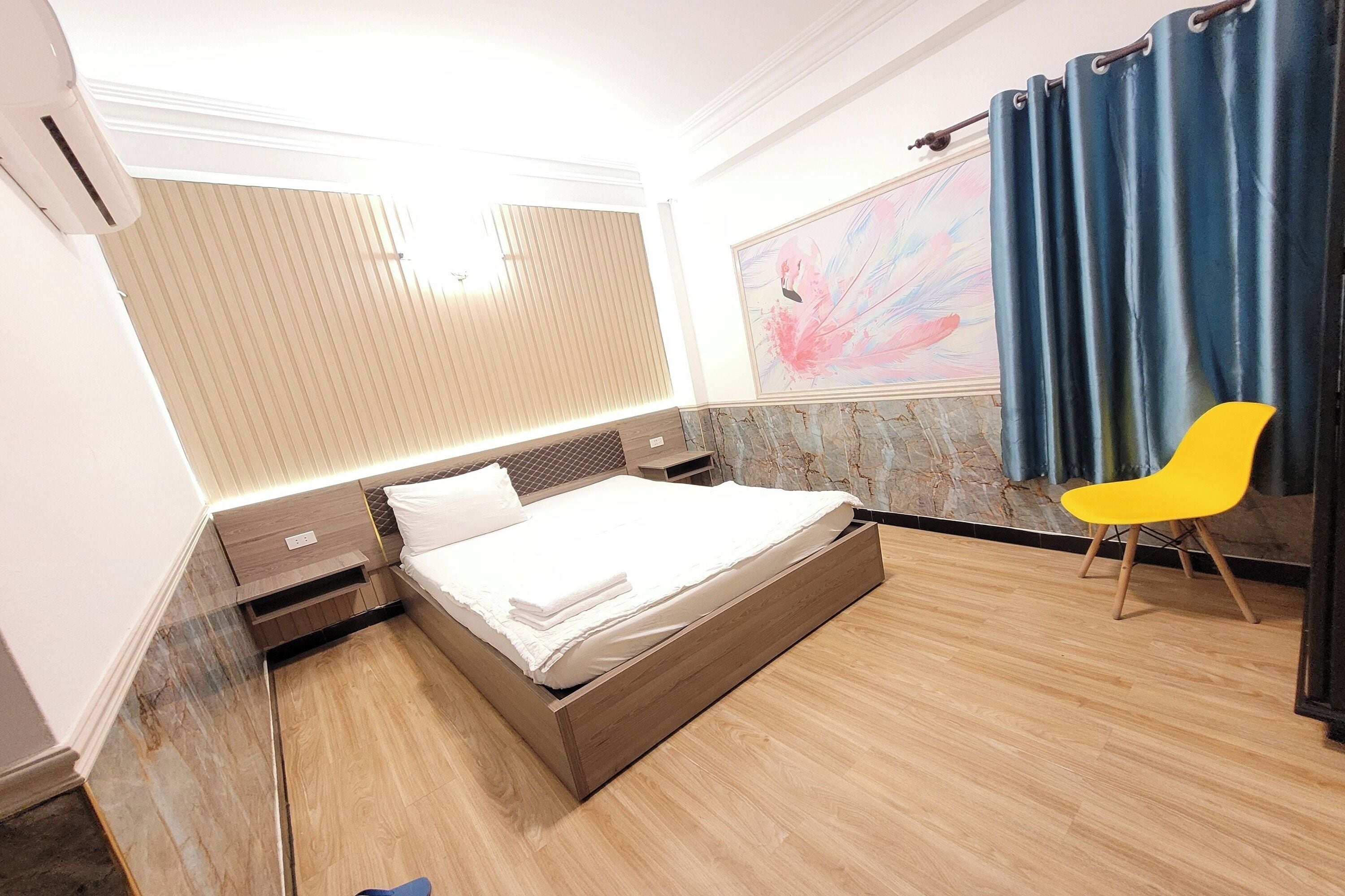 Una habitación de hotel moderna con una cama de madera, una silla amarillo brillante y un cuadro abstracto grande en la pared.