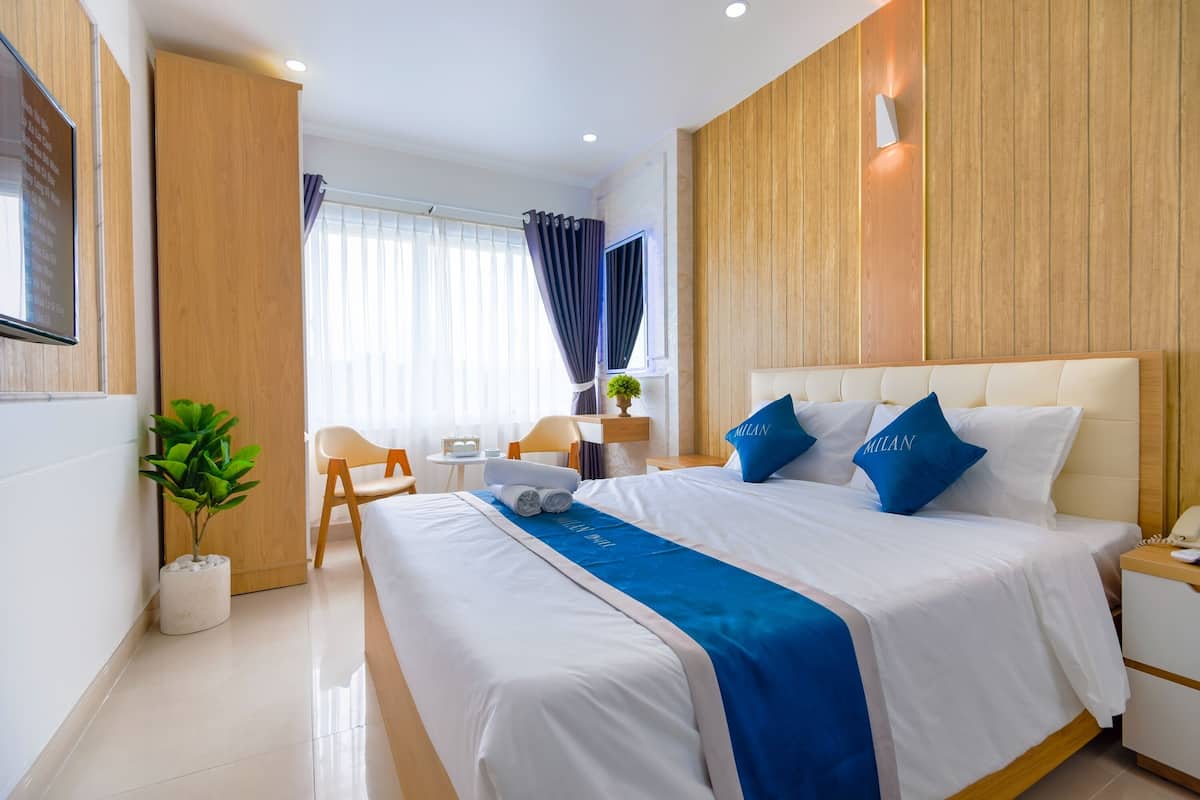 Une chambre d’hôtel moderne avec un grand lit, une table de chevet, un petit bureau et une plante en pot.